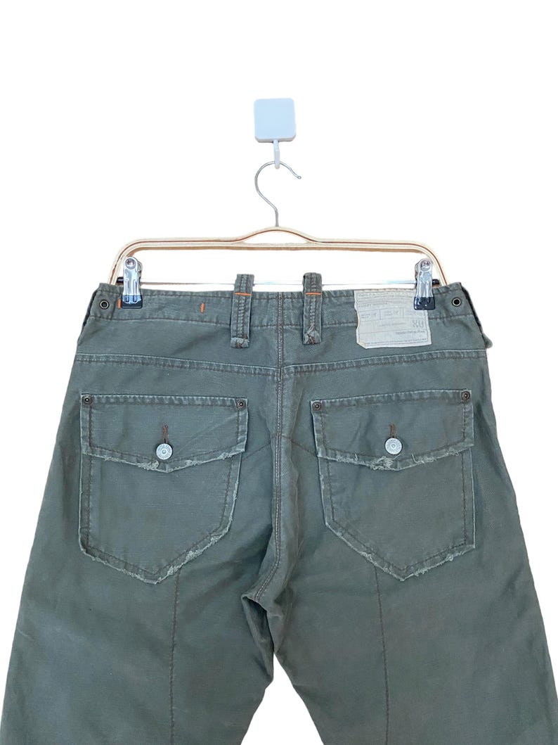 May include: A pair of green cargo trousers with two large pockets on the back. The trousers have a distressed look with frayed edges.