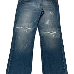 May include: Distressed blue denim jeans with several rips and tears throughout the fabric. The jeans have a classic straight leg fit.