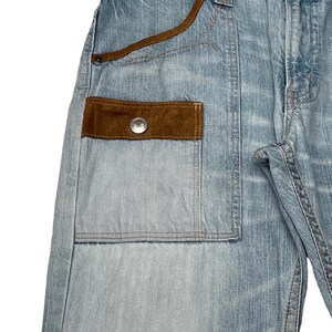May include: Light blue denim jeans with a brown suede patch pocket and a red and black patterned waistband.