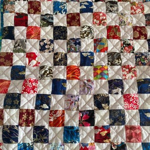 Może przedstawiać: Biała kołdra w kratkę wykonana z kolorowych kwadratów tkaniny. Każdy kwadrat ma inny wzór inspirowany japońską sztuką, w tym wzory kwiatowe, fale i chmury.