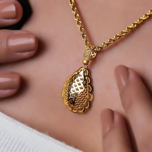 Op de afbeelding: Een gouden ketting met een delicate, ingewikkelde hanger in de vorm van een traan. De hanger heeft een gedetailleerd, opengewerkt ontwerp.