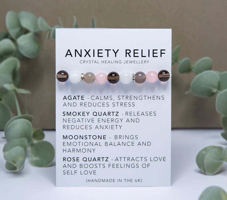 May include: A white card with the text "Anxiety Relief Crystal Healing Jewellery" and a description of the healing properties of agate, smokey quartz, moonstone, and rose quartz. The card also includes a bracelet made with these crystals.