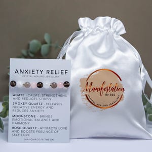 May include: A white satin pouch with the text "Manifestation By S&S Crystal Healing Jewellery" printed on it.  A white card with the text "Anxiety Relief Crystal Healing Jewellery" and a list of crystals and their properties is next to the pouch.