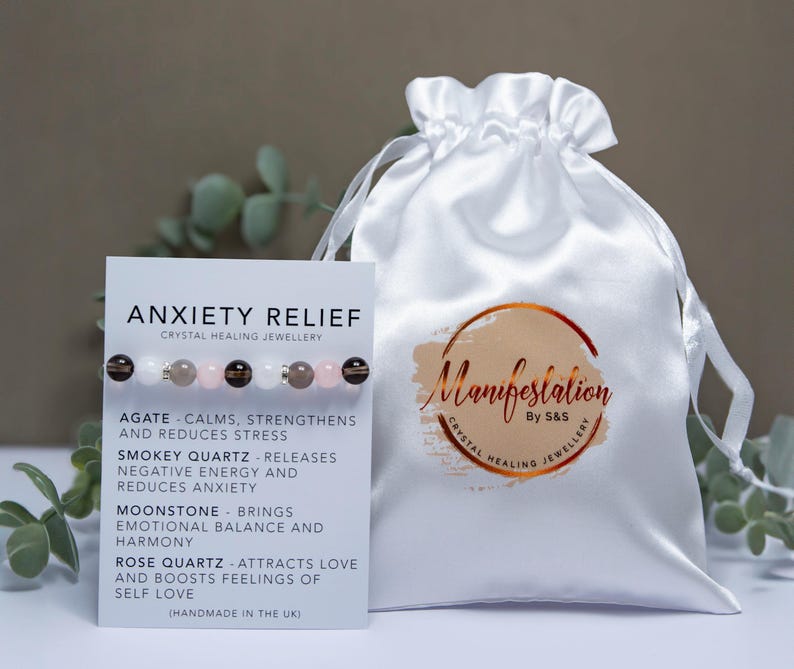 May include: A white satin pouch with the text "Manifestation By S&S Crystal Healing Jewellery" printed on it.  A white card with the text "Anxiety Relief Crystal Healing Jewellery" and a list of crystals and their properties is next to the pouch.