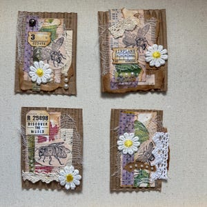 Könnte beinhalten: Vier handgefertigte Collage-Kunstwerke auf Pappe. Jedes zeigt eine Bienenillustration, Stoff, Spitze und eine weiße Gänseblümchen. Ein Stück enthält den Text "DISCOVER THE WORLD".