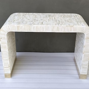 Könnte beinhalten: Ein weißer Konsolentisch mit geschwungenem Design und einer Tischplatte aus eingelegten Perlmutt-Fliesen. Der Tisch hat Messingakzente an den Beinen.