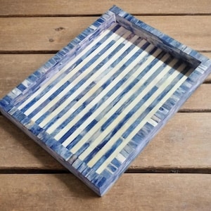 Può includere: Vassoio decorativo rettangolare con motivo a righe blu e bianche. Il vassoio ha un bordo rialzato ed è realizzato con un materiale a mosaico. Il blu ha un effetto marmorizzato. Il vassoio è adatto per servire o esporre.