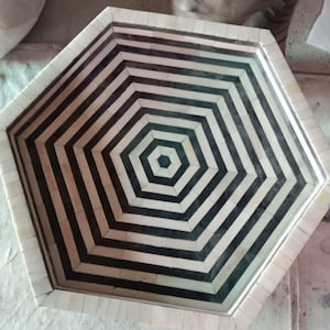 May include: A hexagonal tray with a black and white geometric pattern. The tray is made of bone and has a glass top.