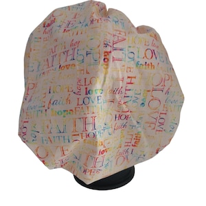 May include: A cream-colored bouffant surgical scrub cap with the words "FAITH," "HOPE," and "LOVE" in a rainbow of colors. The words are repeated across the fabric.
