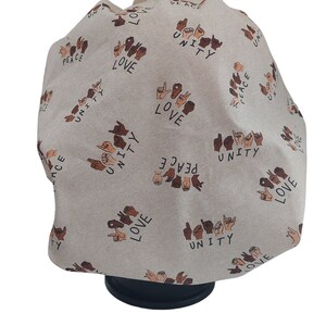 May include: A beige satin bonnet with a repeating pattern of brown hands signing the words "love", "peace", and "unity".