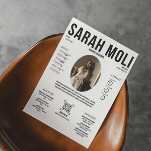 以下が含まれることがあります： 「SARAH MOLI GRAPHIC DESIGNER」というタイトルの白黒の履歴書。写真、スキル、学歴、ポートフォリオ、職務経歴のセクションがあります。履歴書は茶色の革張りの椅子の上にあります。