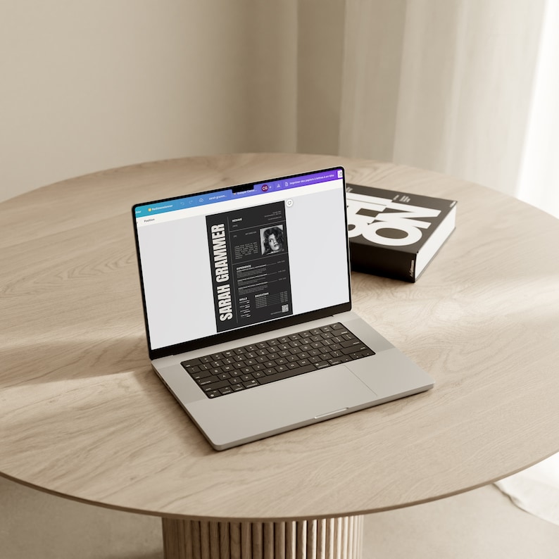 May include: A laptop computer displaying a resume for Sarah Grammer. The resume is in black and white and features a headshot of Sarah Grammer. The laptop is on a light brown wooden table.