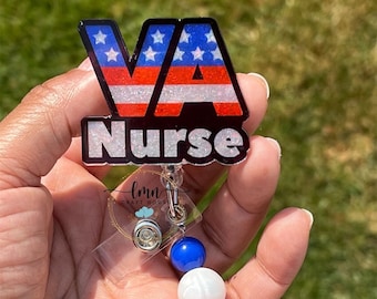 May include: A red, white and blue glitter badge holder with the letters "VA" and the word "Nurse" in white. The badge holder has a clear plastic retractable reel with a blue, white and red bead charm.