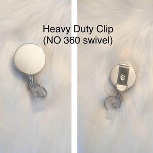 May include: A heavy-duty badge reel with a white face and a silver metal clip. The reel has a clear plastic strap and a metal ring for attaching to a badge. The text "Heavy Duty Clip (NO 360 swivel)" is visible.