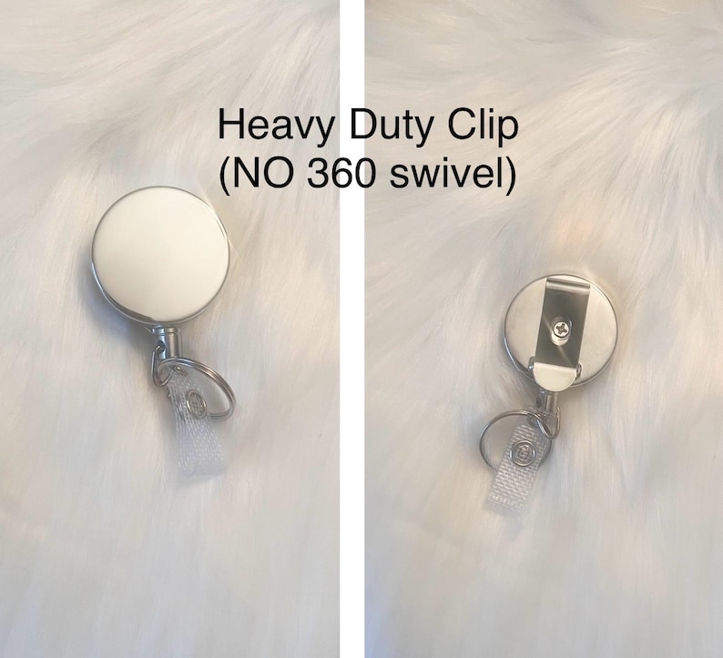 May include: A heavy-duty badge reel with a white face and a silver metal clip. The reel has a clear plastic strap and a metal ring for attaching to a badge. The text "Heavy Duty Clip (NO 360 swivel)" is visible.