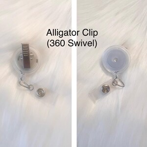 Puede incluir: Un portagafete retr&aacute;ctil de pl&aacute;stico transparente con un clip de cocodrilo plateado y un giro de 360 grados. El texto "Alligator Clip (360 Swivel)" est&aacute; impreso sobre un fondo blanco.