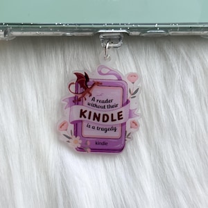 May include: A purple and white phone charm with a dragon and the text "A reader without their Kindle is a tragedy".