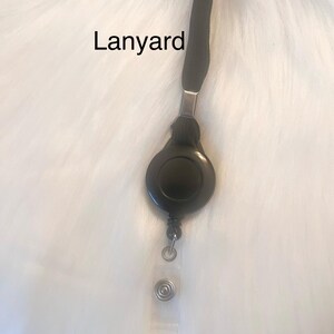 May include: Black lanyard with a retractable badge reel. The reel is round and black, with a clear plastic strap and a metal clip. The word "Lanyard" is printed on the image.