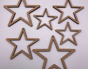 May include: Five wooden star-shaped ornaments of varying sizes. The stars are all cut out, creating a frame-like effect. The stars are a light brown colour.