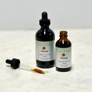 Könnte beinhalten: Zwei dunkle Glasflaschen mit schwarzen Tropfern und weißen Etiketten mit der Aufschrift "Period! Supports menstrual health". Eine Glaspipette mit Flüssigkeit befindet sich neben den Flaschen. Die Flaschen sind 120 ml und 60 ml.