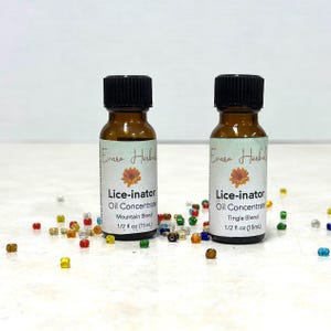 May include: Two small amber glass bottles of "Lice-inator" oil concentrate with black caps. The labels read "Mountain Blend" and "Tingle Blend", each containing 15ml. The brand name "Evara Herbal" is also visible. Colourful beads are scattered around the bottles.