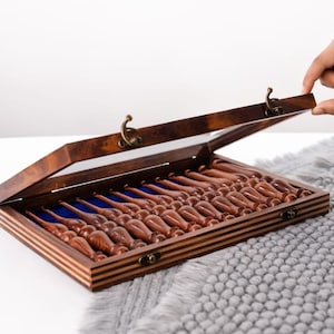Op de afbeelding: Een houten kist met een doorzichtig deksel, gevuld met meerdere bruine objecten. De kist is open, waardoor de inhoud zichtbaar is, en rust op een grijs, getextureerd oppervlak. De kist heeft messingkleurige sluitingen en scharnieren.