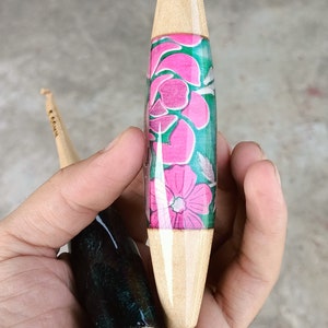 May include: Two wooden crochet hooks with different colored resin handles. One hook has a pink and green floral design, the other has a black and green marbled design.