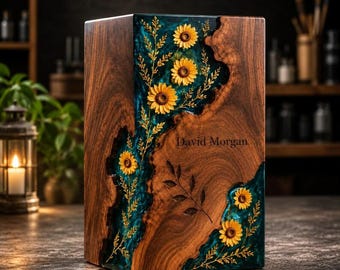 May include: A rectangular wooden urn featuring a central vertical inlay of translucent teal resin. The resin section contains embedded yellow sunflower heads and delicate golden foliage. The name David Morgan is engraved on the wood surface.