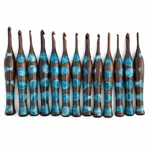 Peut inclure: Une collection de dix crochets en bois, avec une finition marron foncé et des accents de résine bleu turquoise. Les crochets sont disposés en rangée sur un fond blanc, mettant en valeur leur design unique et leur savoir-faire. Chaque crochet a une forme distincte.