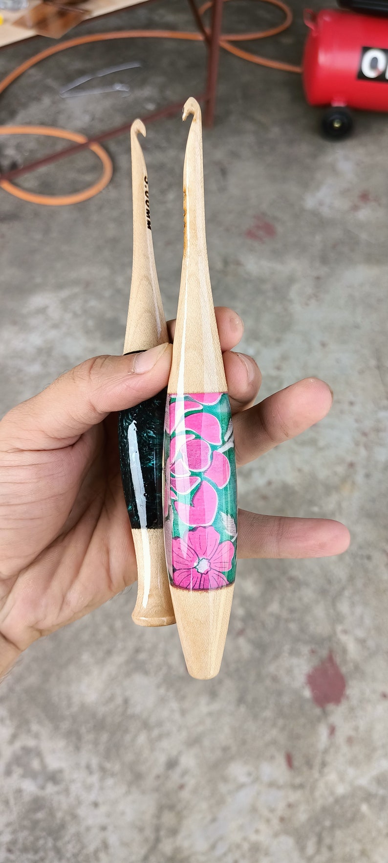 May include: Two wooden crochet hooks with different colored handles. One hook has a black and green handle with the word "SUMMUM" written on it. The other hook has a pink and green floral design on the handle.