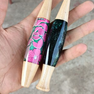 May include: Two wooden crochet hooks with different colored handles. One hook has a pink and green floral design, and the other has a black and green marbled design. The hook with the floral design is labeled "5.00mm" and the other hook is labeled "5.00mm".