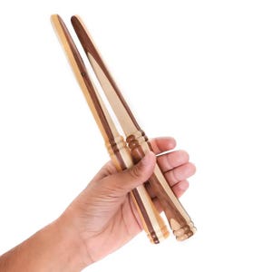 May include: Two wooden knitting needles with a brown and light wood pattern. The needles are held in a hand.