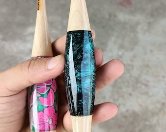 May include: Two wooden crochet hooks with different colored handles. One hook has a teal and black handle, the other has a pink and green floral design. Both hooks have the size marked on them.