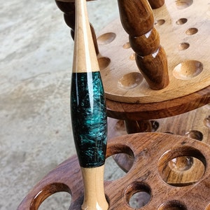 May include: A wooden crochet hook stand with a teal and black crochet hook. The hook is labeled "5.00 MM".