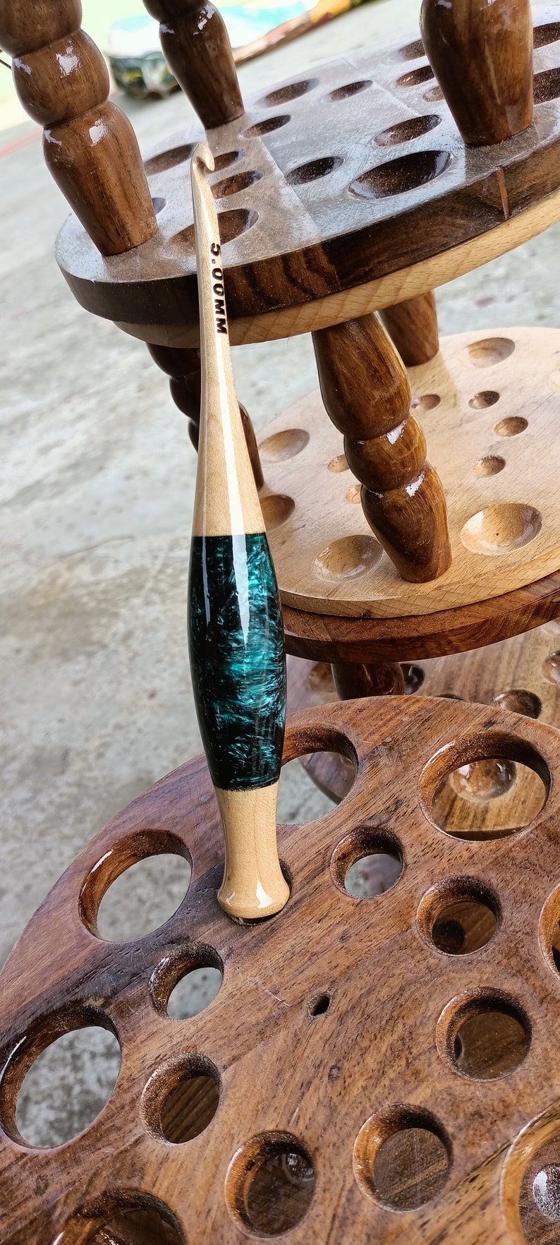 May include: A wooden crochet hook stand with a teal and black crochet hook. The hook is labeled "5.00 MM".