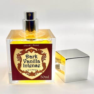 May include: A clear, square perfume bottle with a silver cap and a label that reads "Dark Vanilla Intense" by Juliet Rose. The label is burgundy with gold accents and the bottle contains 50ml of perfume.