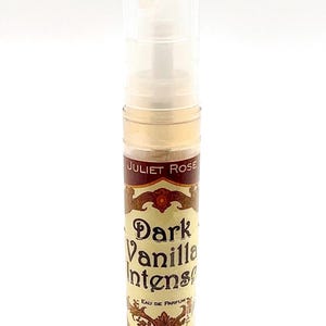 May include: A clear glass vial of "Dark Vanilla Intense" eau de parfum by Juliet Rose. The label is brown and gold with ornate lettering. The vial has a clear plastic cap and contains a light amber liquid.