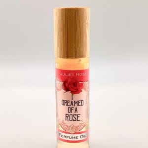 Könnte beinhalten: Eine kleine Glasflasche mit einem Bambusdeckel und einem rosa-goldenen Etikett. Das Etikett lautet "Juliet Rose Dreamed of a Rose Perfume Oil".
