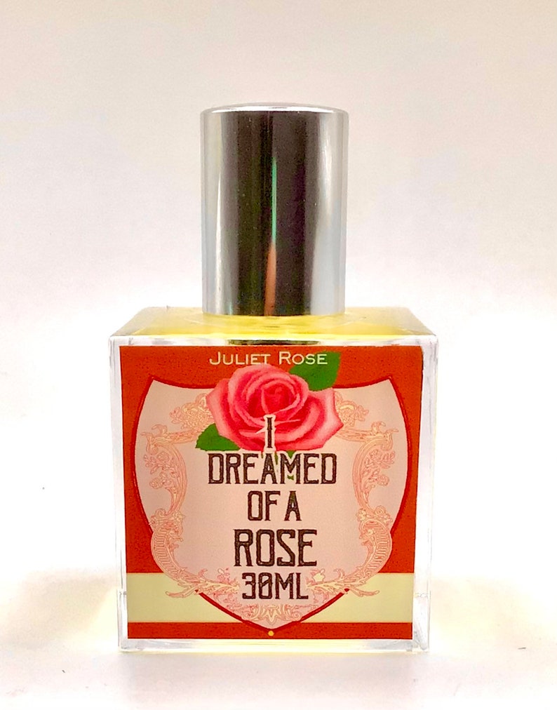 Puede incluir: Una botella de vidrio transparente con una tapa plateada y una etiqueta que dice "JULIET ROSE I DREAMED OF A ROSE 30ML". La etiqueta es naranja con una ilustraci&oacute;n de rosa rosa.