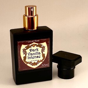 May include: A black rectangular perfume bottle with a gold cap and a detached black cap. The label reads "Dark Vanilla Intense" and "30ml". The bottle is from "Juliet Rose".