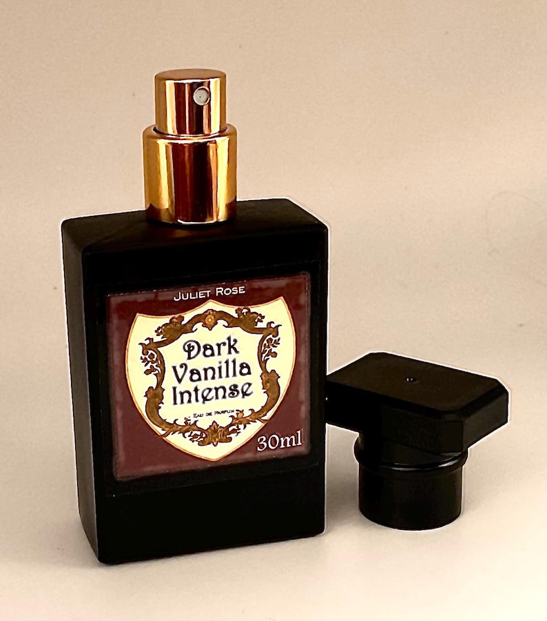 May include: A black rectangular perfume bottle with a gold cap and a detached black cap. The label reads "Dark Vanilla Intense" and "30ml". The bottle is from "Juliet Rose".