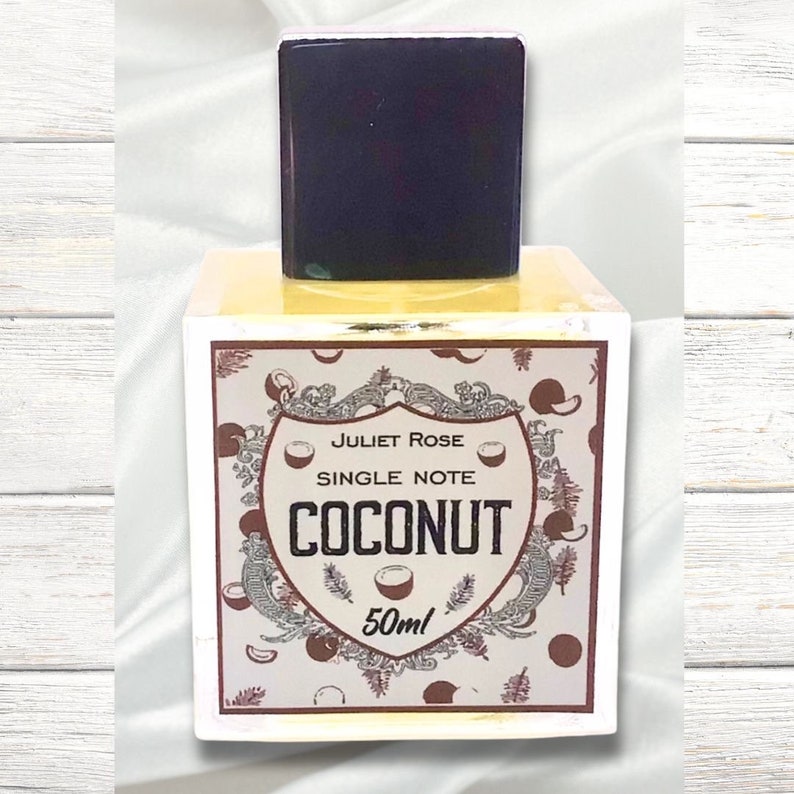 May include: A yellow glass bottle with a black cap and a label that says "Juliet Rose Single Note Coconut 50ml". The label has a brown and white design with coconuts and leaves.