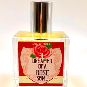 Puede incluir: Una botella de vidrio transparente con una tapa plateada y una etiqueta roja. La etiqueta presenta una rosa rosa y el texto "I DREAMED OF A ROSE 50ML" en letras negras. El texto "JULIET ROSE" est&aacute; impreso en negro en la parte superior de la etiqueta.