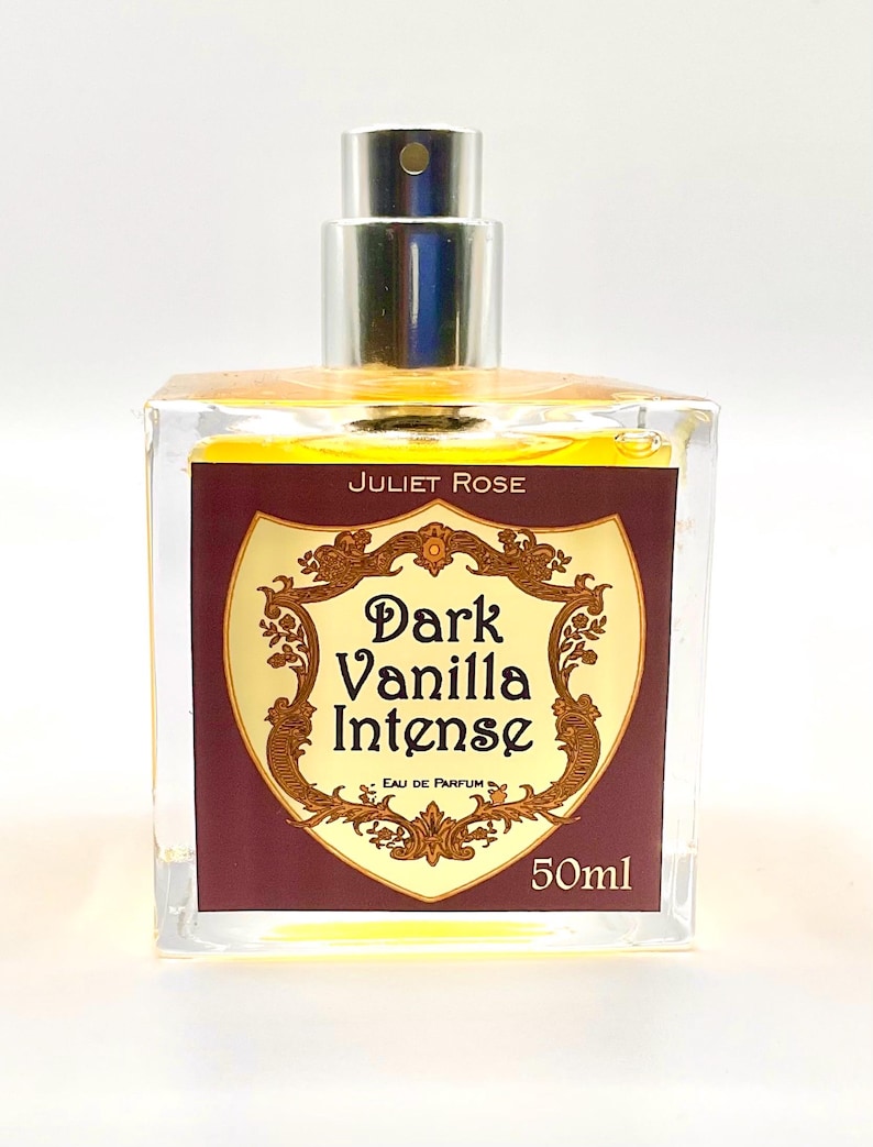 May include: A clear glass perfume bottle with a silver cap. The label reads "Juliet Rose Dark Vanilla Intense Eau de Parfum 50ml" in gold lettering on a burgundy background. The perfume inside is a golden colour.