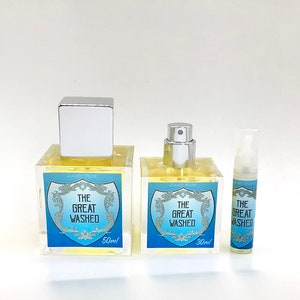 May include: Three perfume bottles of varying sizes. The bottles are clear with a light yellow liquid inside. Each bottle has a label with the text "THE GREAT WASHED" on a blue background. The largest bottle is 50ml, the middle is 30ml, and the smallest is a sample size.