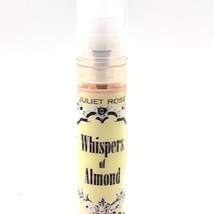Puede incluir: Un pequeño frasco de perfume con tapón transparente. La etiqueta dice "JULIET ROSE Whispers of Almond". El frasco tiene una etiqueta amarilla clara con elementos decorativos y texto en negro. El líquido interior es de color ámbar claro.