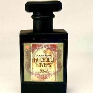 May include: A rectangular black perfume bottle with a matching black cap. The front label features a decorative illustration of a person, the text "JULIET ROSE", "PATCHOULI LOVERS", and "30ml", along with a small pink heart icon in the corner.
