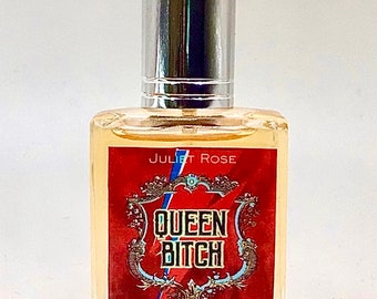 May include: A clear glass bottle of perfume with a silver cap. The label is red with gold trim and says "Queen Bitch" with a lightning bolt design. The text "Juliet Rose" is printed in white on the label.