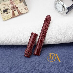 May include: Two red leather watch straps with a textured finish. The straps are on a white surface with a blue surface underneath.