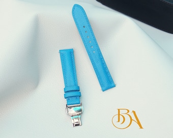 May include: Two light blue leather watch straps with a silver buckle. The straps are laid out on a white surface.